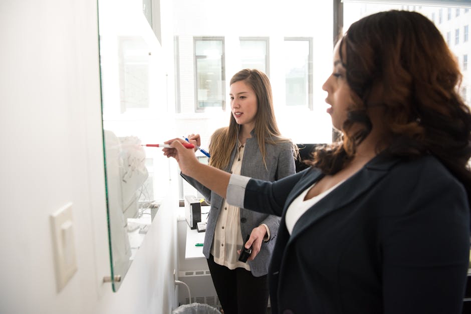 A diverse group of people brainstorming and discussing ideas on a whiteboard, with one person writing down notes.