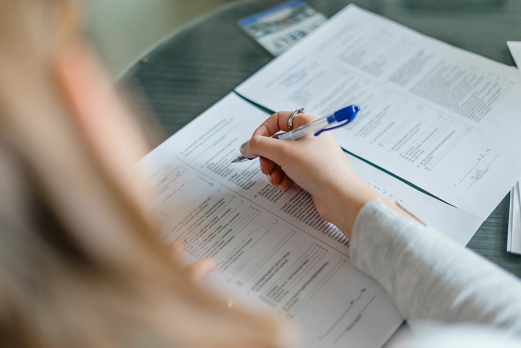 A person filling out business registration forms and documents on a desk, surrounded by pens and a laptop.