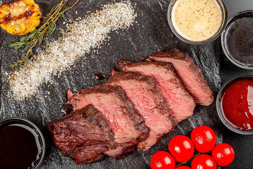 Eine Auswahl an verschiedenen Fleischsorten wie Steak, Hühnchen und Schweinefleisch, dekorativ angerichtet mit einer Vielzahl an Hot Sauce-Flaschen