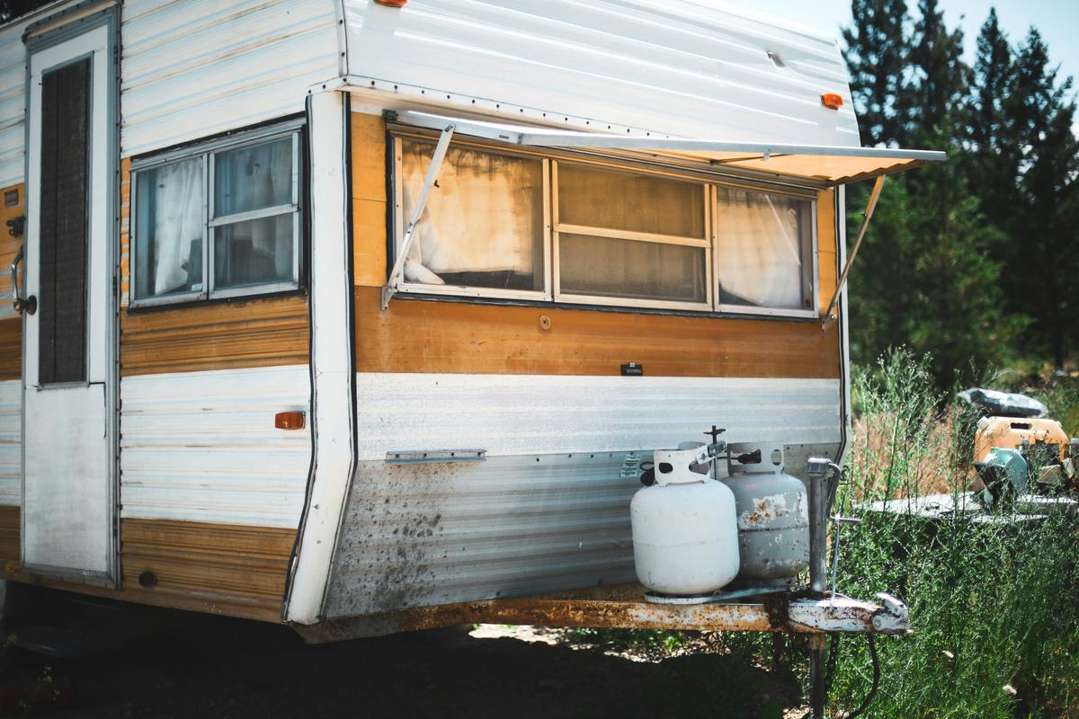 An image of an RV parked at a gas station, with the fuel pump inserted into the tank and propane tanks visible on the side of the vehicle