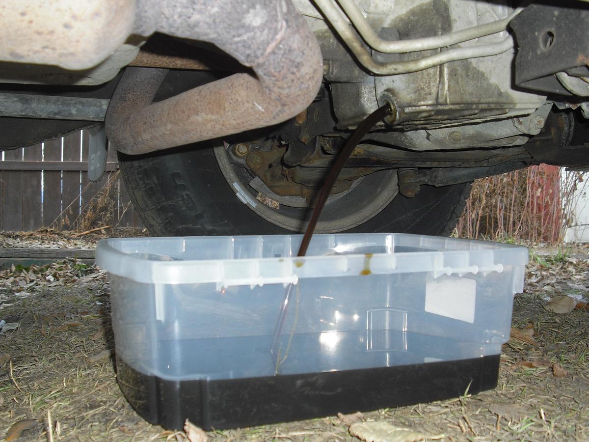 A mechanic draining the old oil from a vehicle's engine by removing the drain plug and allowing the oil to flow into a drain pan.