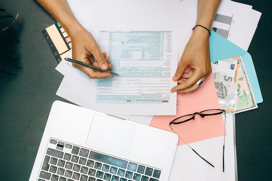 A photo of a person sitting at a desk with a laptop open, reviewing tax documents and using online tax filing software.