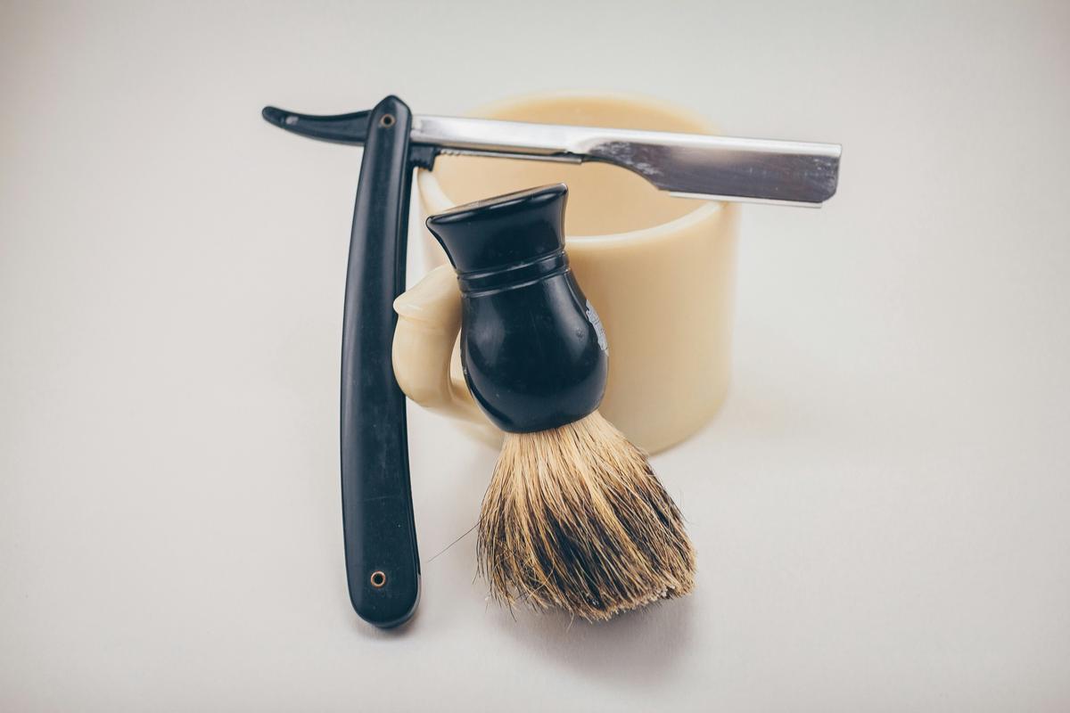 An image showing various traditional wet shaving tools and products on a wooden shelf