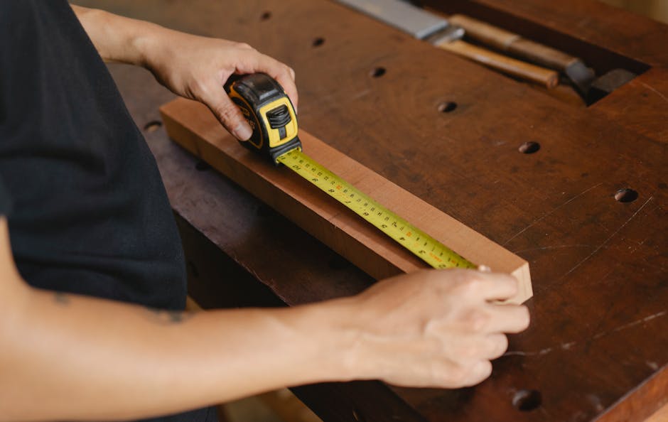 A woodworker carefully measuring a piece of wood with a ruler and marking it with a pencil.